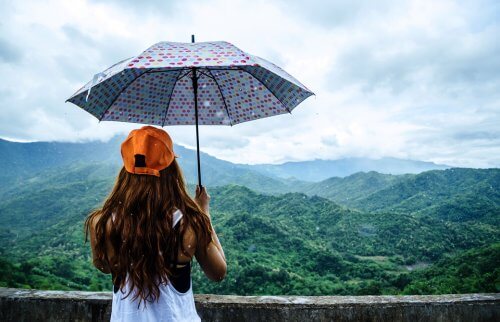 雨の中を美しい山並みに向かって傘をさしている女性の後ろ姿 Rainy Season ヨガジェネレーション Yogageneration