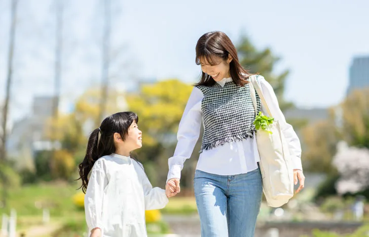 手を繋いで歩きながら子供に向かって微笑む女性